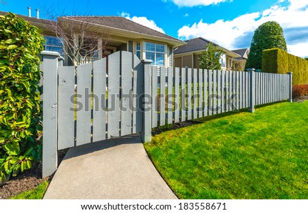 Country style long wooden fence with the gate, wicket and a house behind. Country style long wooden fence with nicely trimmed grass.