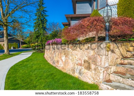 Leveled and stoned curved front yard with some flowers and nicely trimmed bushes and grass. Landscape design.