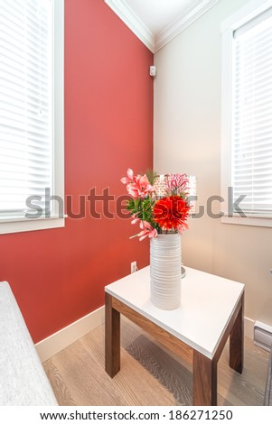 Fragment of a luxury living suite. Nicely decorated modern family, living room with decorative vase with some flowers on the coffee table and red colored room. Interior design. Vertical.