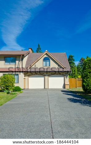 Big custom made double doors garage with nicely paved long and wide driveway in the suburbs of Vancouver, Canada. Vertical.
