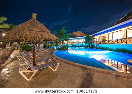 Beach grass umbrella at swimming pool and a restaurant of luxury caribbean resort at night, dawn time. Bahia Principe, Riviera Maya, Mexico.