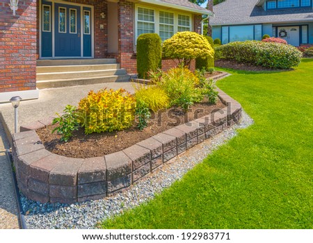 Nicely decorated colorful flowerbed, front yard, lawn with stones and bushes as a decorative elements. Landscape design.