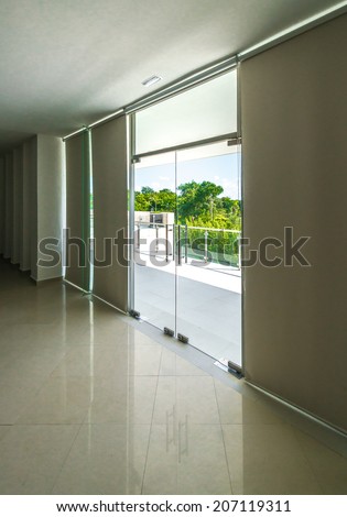 Outlook, view from inside through the glass doors to the modern glass and steel balcony, deck, patio, promenade railing. Exterior, interior design. Vertical.