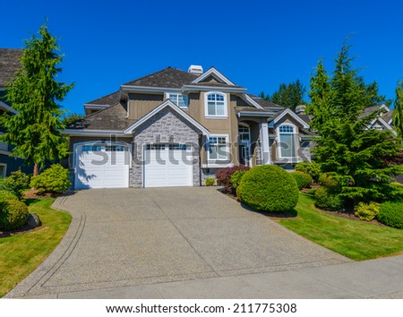 Big custom made luxury house with nicely landscaped front yard and long and wide driveway to garage in the suburbs of Vancouver, Canada.