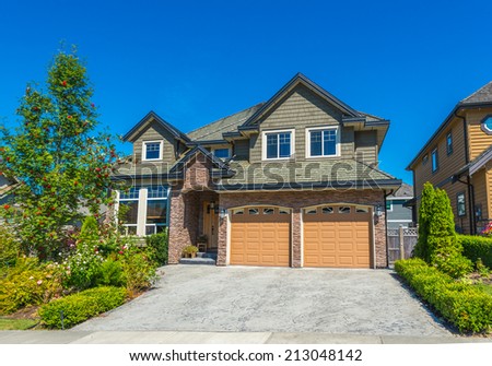 Big custom made luxury house with nicely landscaped front yard and paved driveway to garage in the suburbs of Vancouver, Canada.