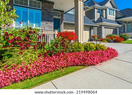 Nicely decorated colorful flowerbed and trimmed front yard lawn in front of the house at the pedestrian sidewalk. Landscape design.