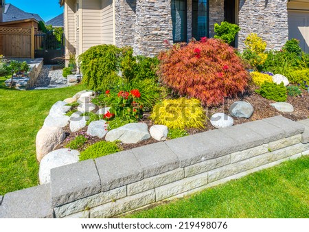 Nicely decorated colorful flowerbed and trimmed bushes at front yard lawn in front of the house. Landscape design.