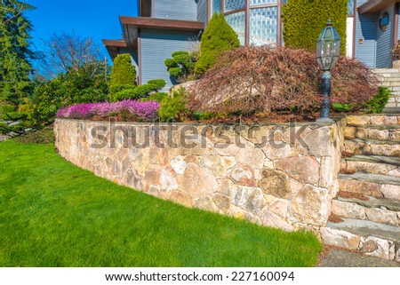 Leveled and stoned curved front yard with some flowers and nicely trimmed bushes and grass. Landscape design.d