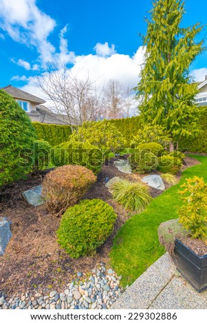 Nicely trimmed and landscaped front, back yard. Flowers and stones in front of the house, front yard. Landscape design. Vertical.