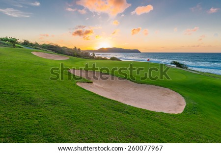Red flag and sand bunkers at the beautiful golf course at the ocean side at sunset, sunrise time.