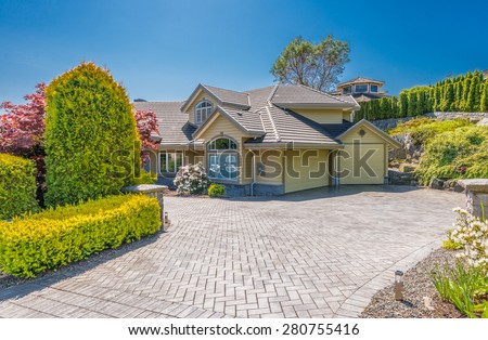 Custom built luxury house with nicely trimmed front yard, lawn and paved driveway to garage in a residential neighborhood. Vancouver Canada.