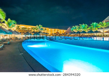 Swimming pool and a grass beach umbrellas with lounges at night, dawn time. Mexico.