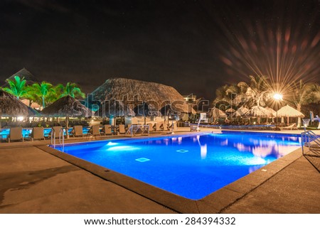 Swimming pool and a grass beach umbrellas with lounges at night, dawn time. Mexico.