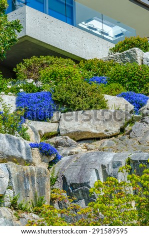 Trimmed bushes, flowers and stones in nicely decorated front yard. House on the rocks. Landscape design. Vertical.