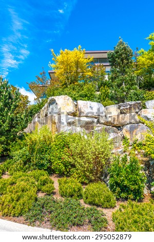 Flowers, stones and nicely trimmed bushes in front of the house, front yard. Landscape design. Vertical.