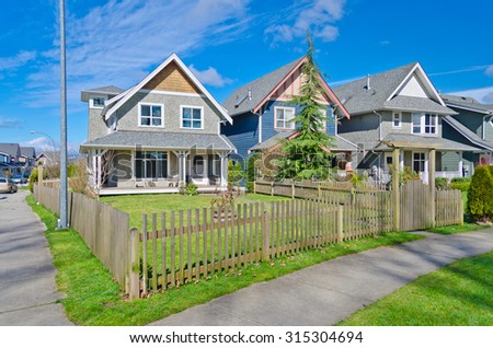 Comfortable neighborhood. Some middle class homes with nicely landscaped front yard lawn behind the wooden fence in the suburbs of the North America. Canada.
