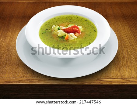 Hot vegetarian healthy soup with pesto sauce, noodles and vegetables in a round plate on wooden table