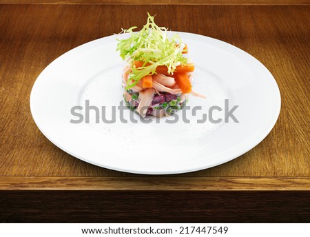Fresh tasty Russian salad served with carrots and green salad leaf. Wooden table