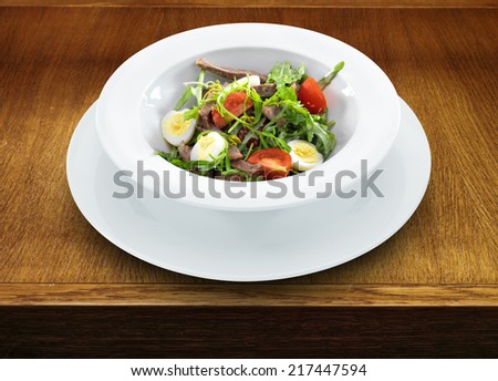 Warm delicious italian salad with beef tongue and arugula on a white round plate on wooden table