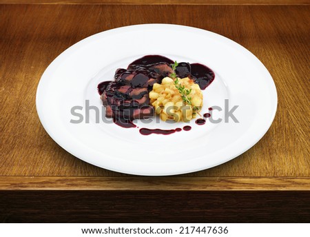 Delicious roasted sliced duck breast meat under wine and berry sauce with apples on the white plate on wooden table