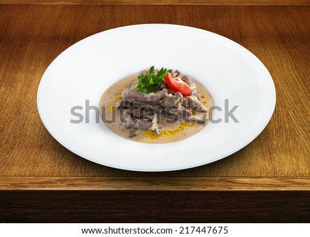 Delicious hot beef stroganoff with cream sauce served on a white plate. Wooden table