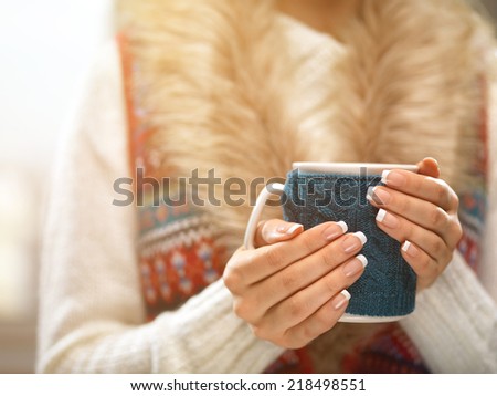 Woman holds a winter cup close up. Woman hands with elegant french manicure nails design holding a cozy knitted mug. Winter and Christmas time concept.