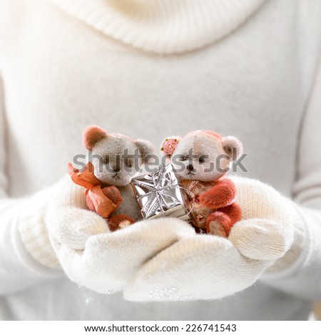 Female hands holding a cute teddy bears with gift. Woman hands in white mittens showing a teddy bear gift. Cute Christmas present. Winter holidays concept.