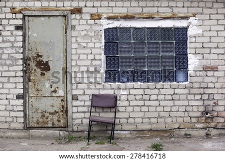 Brick wall with glass bricks window, rusted doors, old chair .
