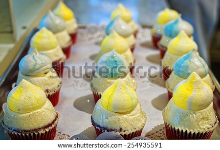 Creamy cupcakes with coloured domes on the bakery storefront with blurred background