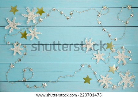 Frame of  white crocheted snowflakes and golden stars on a blue wooden background.