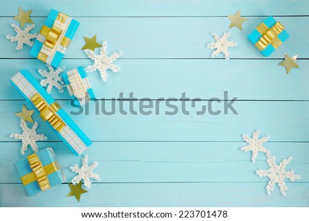 Five scattered gift boxes with golden bows and crocheted snowflakes on a blue wooden background top view.