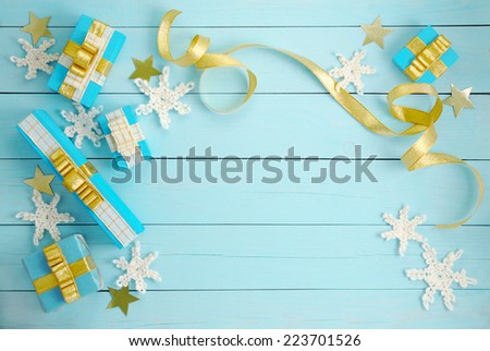 Five scattered gift boxes with golden bows and crocheted snowflakes on a blue wooden background.