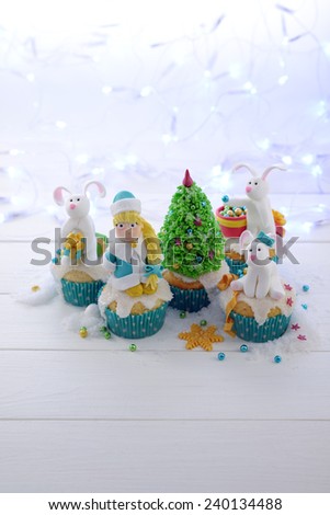 Festive cupcakes with sugar figures on a bright lights background vertical format. Snow Maiden and rabbits decorating the Christmas tree.