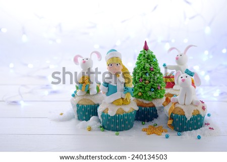 Festive cupcakes with sugar figures on a bright lights background. Snow Maiden and rabbits decorating the Christmas tree.
