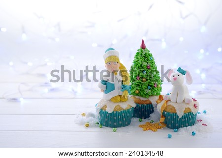 Festive cupcakes with sugar figures on a bright lights background. Snow Maiden Christmas tree and a rabbit in a blue bow.