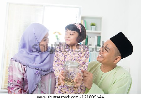 Southeast Asian family. Muslim girl hand holding money jar at home.
