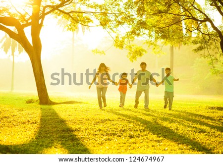 Southeast Asian Chinese family holding hands, running at outdoor green park during sunrise