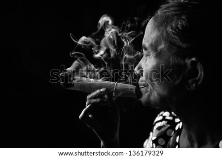 Old wrinkled Asian woman smoking traditional tobacco in monotone, black and white portrait. Bagan, Myanmar.