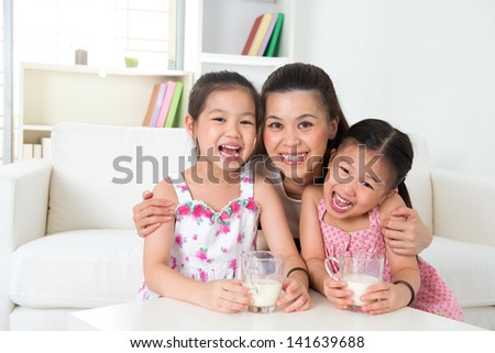 Happy Asian mother and daughters drinking milk at home. Parent and children. Beautiful family model.