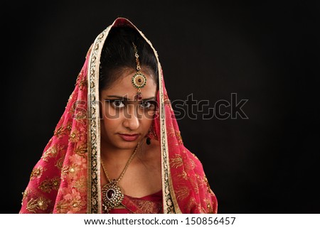 Head shot of beautiful young Indian woman in traditional sari dress, veil covering head, isolated on black background.