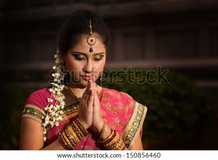 Portrait of beautiful young Indian woman in traditional sari dress praying in a hindu temple.