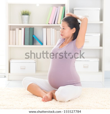 Pregnancy yoga meditation. Full length healthy 8 months pregnant calm Asian woman meditating or doing yoga exercise at home. Relaxation yoga stretching positions.