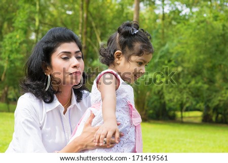 Happy Indian family at garden park. Portrait of a mother helping baby girl to walk outdoor.