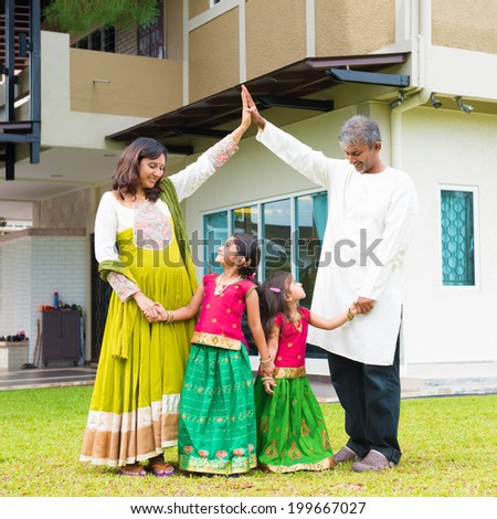 Parents forming  house roof shape above children. Beautiful Asian Indian family portrait smiling and standing outside their new house.