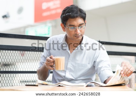 Asian Indian businessman reading newspaper while drinking a cup hot milk tea during lunch hour at cafeteria.