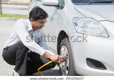 Asian Indian driver checking air pressure and filling air in the tires of his car.
