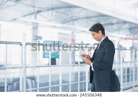 Asian Indian businessman using tablet computer while waiting train at railway station.