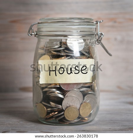 Coins in glass jar with house label, financial concept. Vintage wooden background with dramatic light.