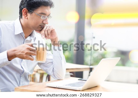 Man using laptop computer while drinking a cup hot milk tea, outdoor cafe.