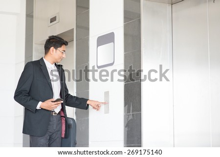 Young Indian businessman pressing on elevator button, waiting door open to enter inside the lift.